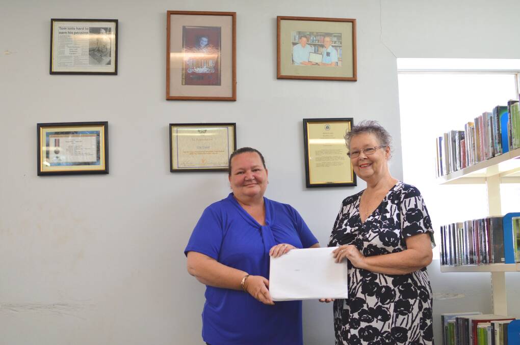 LEAVING A LEGACY: Library manager Colleen Kerr accepts the bequeathment of shares from Katherine Community Bank's Merrilyn Stopp in front of Tom's Wall last week.